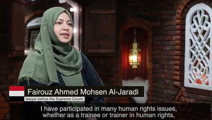 A woman in a green hijab speaks on camera in a lantern-lit brick interior; on-screen text reads "lawyer before the Supreme Courts" and a caption about participating in human rights work.