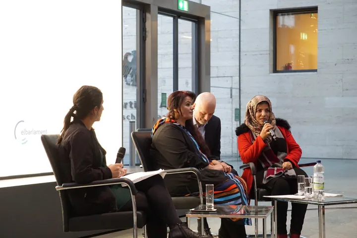 Four women seated in a panel discussion, one speaking into a microphone, with the elbarlament logo displayed on a screen beside them.