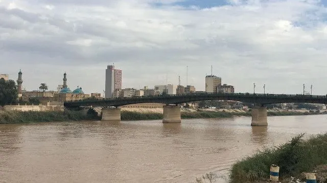 A river with a bridge, mosque minarets and domes, and a city skyline under a cloudy sky.