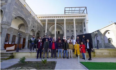 Group photo of people standing on the steps of a historic stone building with columned arches under a blue sky.