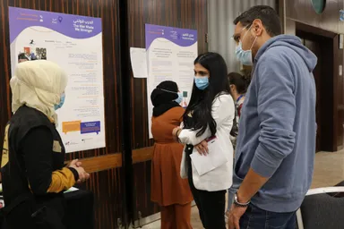 Four people wearing face masks stand together looking at posters reading "The War Made Me Stronger" and "The Echo of Change".