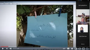 Paused video call recording showing a paper sign with Arabic text, including "حكايات بلا بيوت", clipped to a tree branch, with a participant panel and playback controls on screen.
