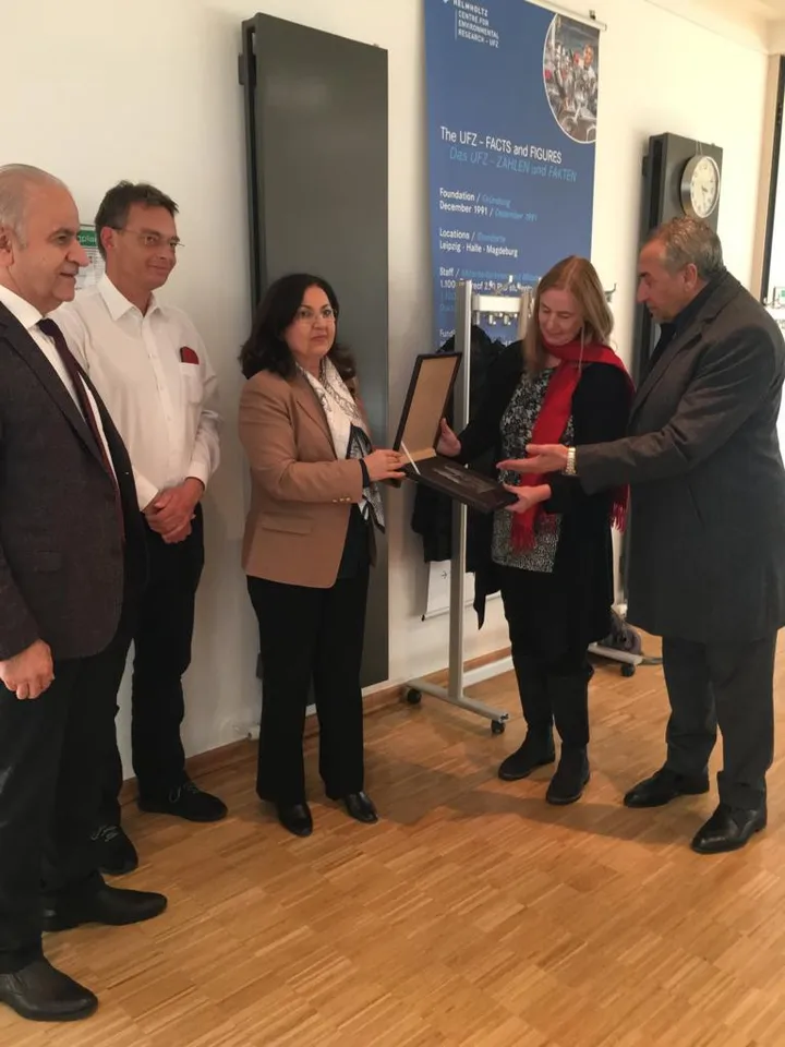 Five people stand in an office as one hands another a framed plaque, in front of a banner reading "THE UFZ - FACTS AND FIGURES" for the Helmholtz Centre for Environmental Research.