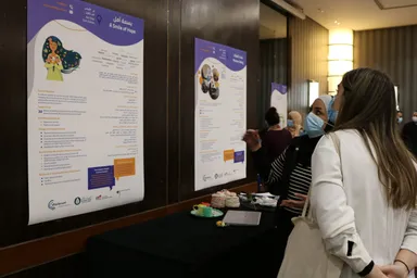 People wearing face masks look at exhibition posters, one reading "A Smile of Hope" and "بسمة أمل" with an illustration of a woman holding flowers.