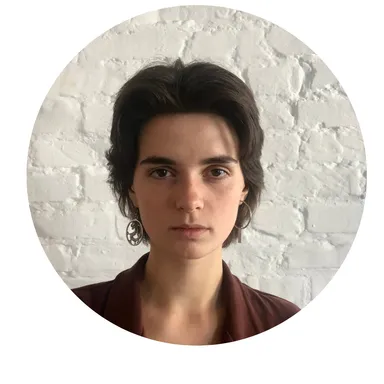 Black-and-white circular portrait of a woman with short dark hair and hoop earrings against a brick wall.