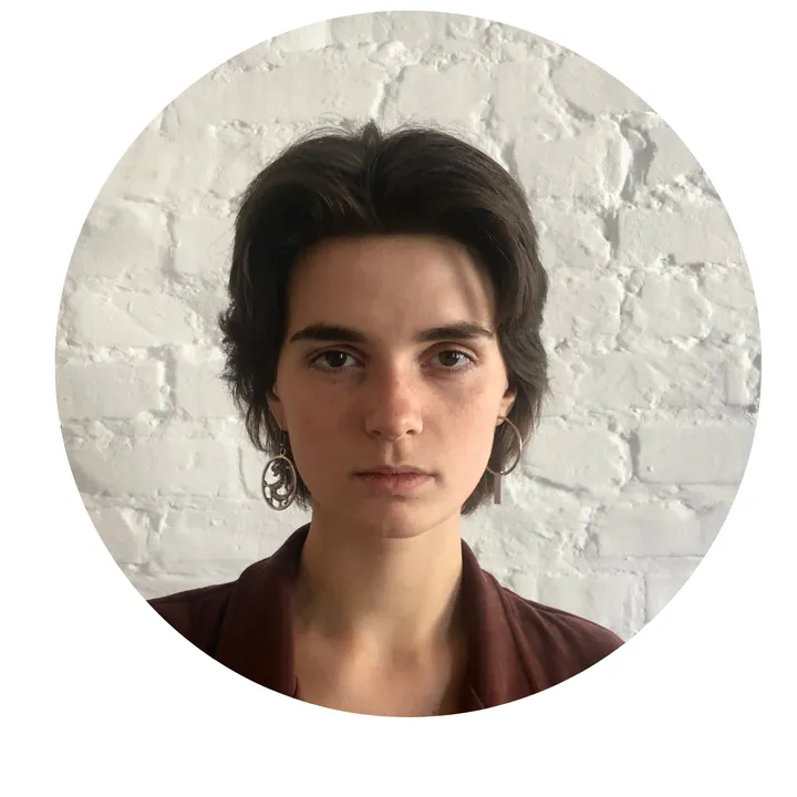 Black-and-white circular portrait of a woman with short dark hair and hoop earrings against a brick wall.