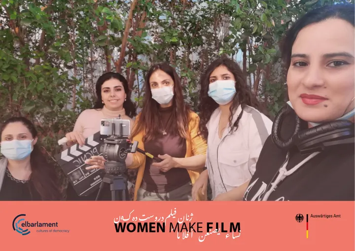 Five women wearing face masks stand outdoors, one holding a clapperboard, under a banner reading "WOMEN MAKE FILM" with the elbarlament and Auswärtiges Amt logos.