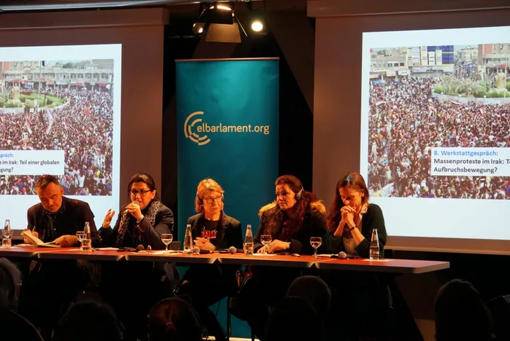 Five people sit at a panel discussion table between two screens showing crowd photos, in front of a banner reading "elbarlament.org".