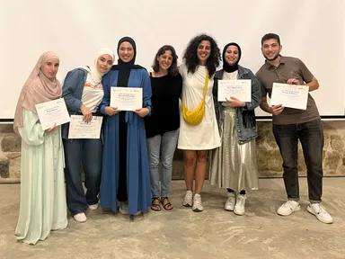 A group of people holding "Certificate of Participation" papers, posing together in front of a stone wall.