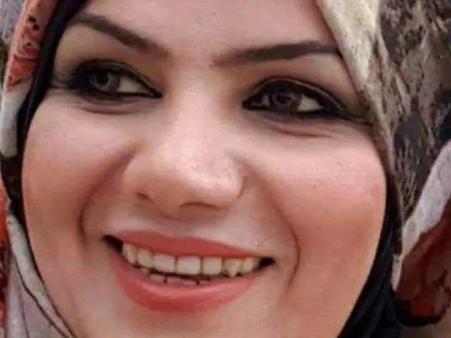 Extreme close-up of a woman's face, smiling, wearing a headscarf with a floral and striped pattern.