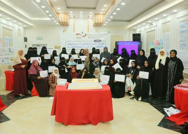 A group of women in a conference hall hold certificates around a table with a cake, in front of a banner with Arabic text and small "german cooperation" and "giz" logos.