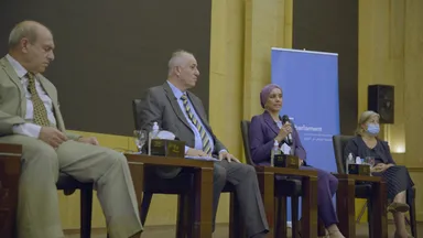 Four panelists sit at a table, a woman in a headscarf speaking into a microphone, with an "elbarlament" banner in the background.