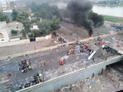 Aerial view of a debris-covered overpass with black smoke rising from a fire and a flag lying among the wreckage.