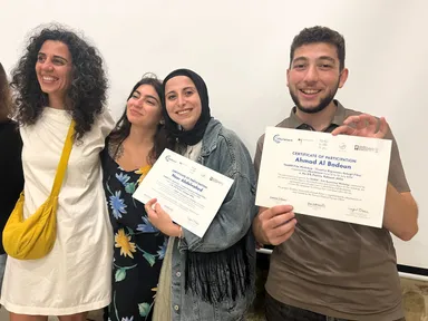Four people smiling while holding "Certificate of Participation" documents indoors.