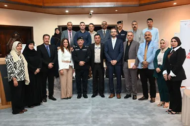 A group of people, including one in a police uniform, standing together indoors for a group photo, with event banners in the background.