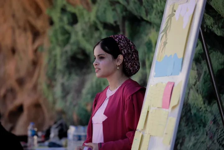 A woman in a headscarf stands smiling beside a flipchart covered with colorful notes.