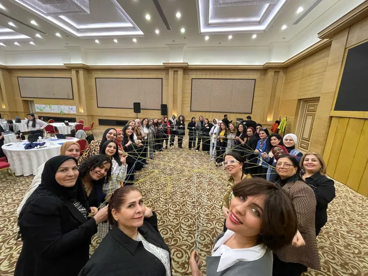 A large group of women in a conference hall holding strands of string that form a web pattern between them.