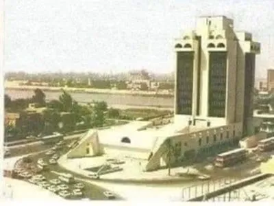 Aerial view of a modern government building complex beside a river, with cars and buses parked along the surrounding roads.