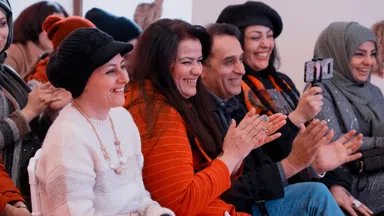 A group of people smiling and applauding, one holding up a phone on a selfie stick.