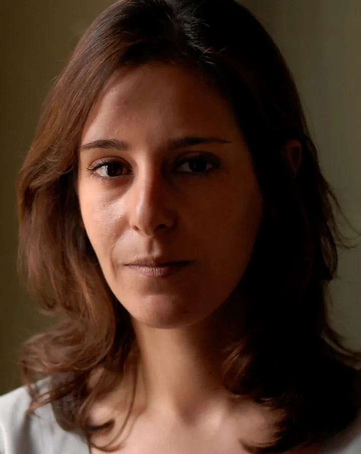 Close-up portrait of a woman with long brown hair in dim lighting, looking to the side.
